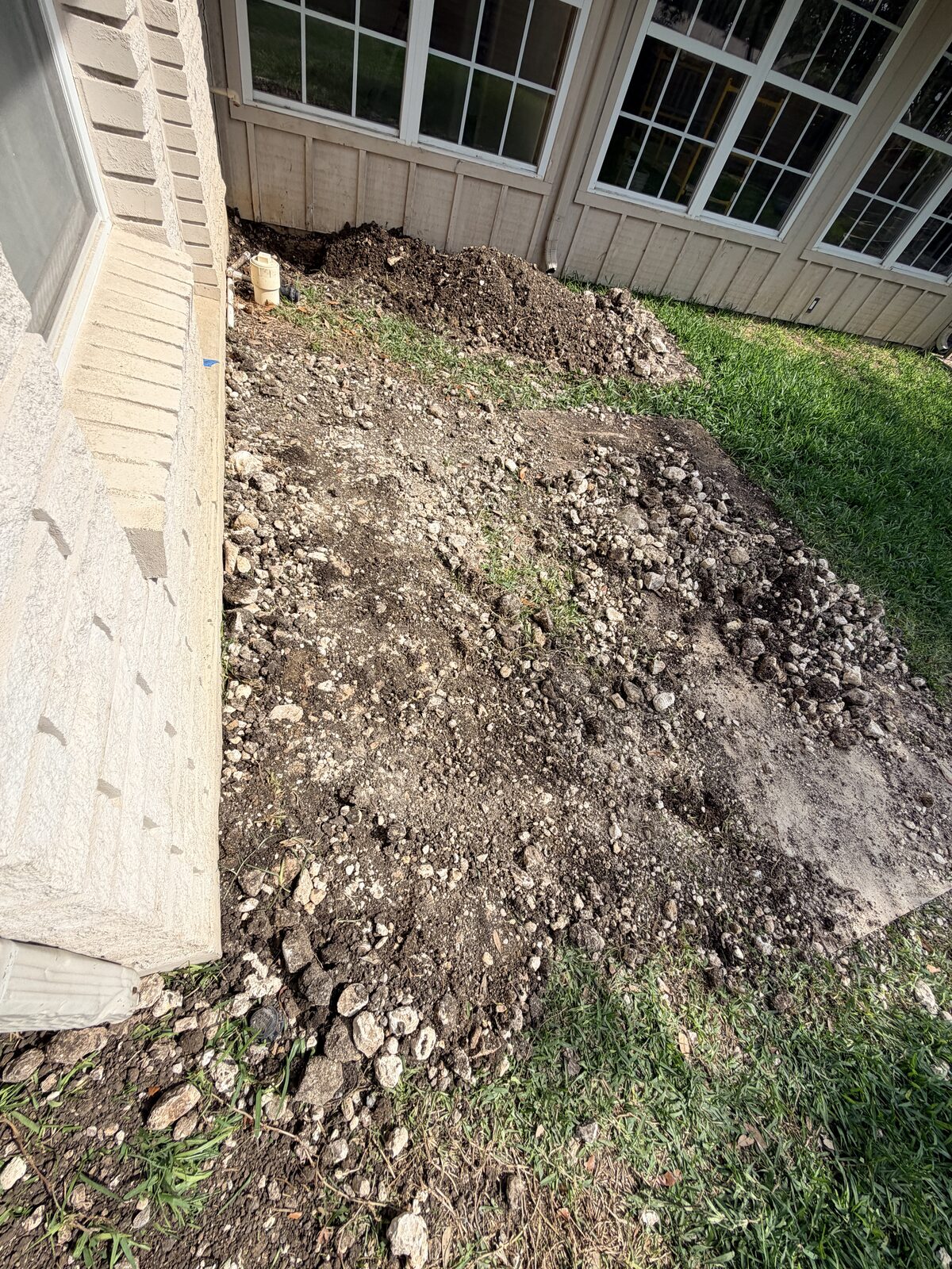 Freshly backfilled soil along a home's foundation after pier installation and excavation work