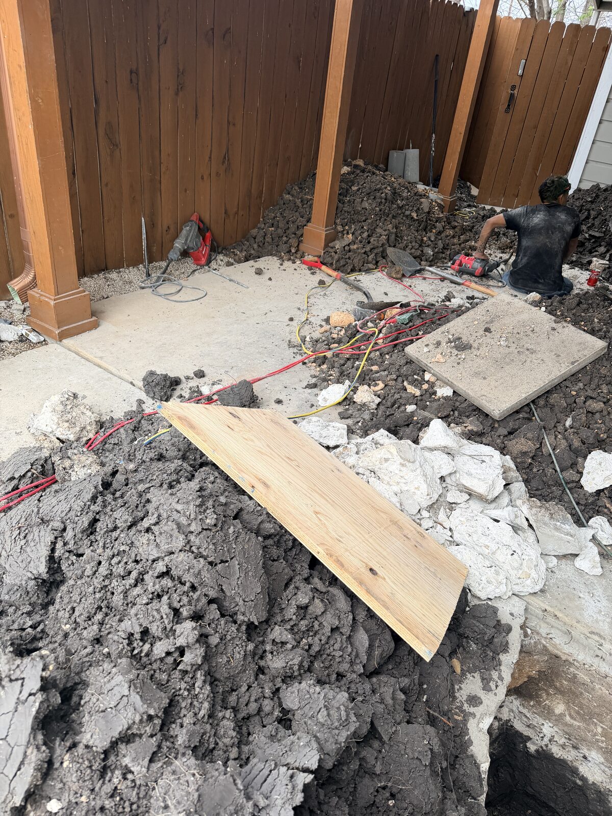 Backyard foundation repair site with spoil piles and plywood walk boards during pier excavation