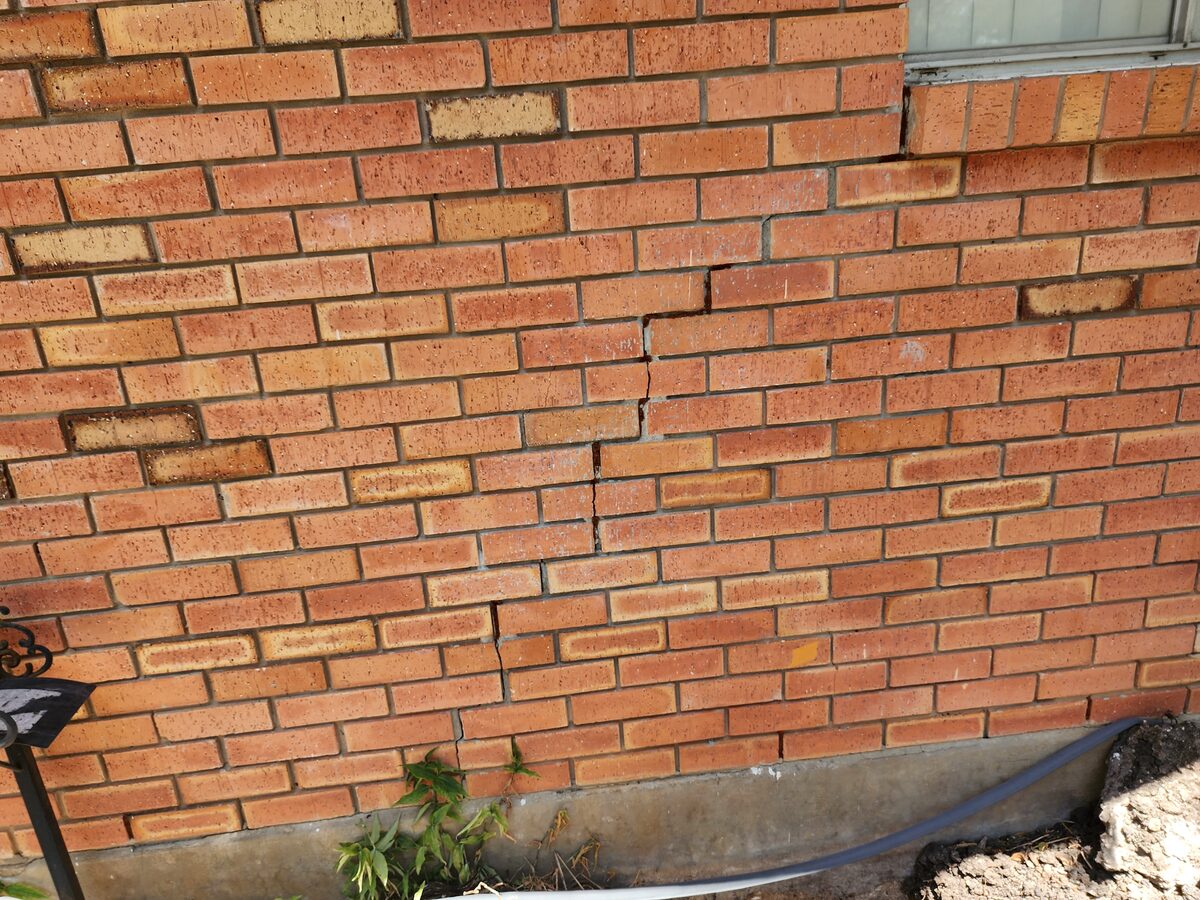 Stair-step and vertical cracks in red brick veneer beneath a window, with the foundation exposed for repair