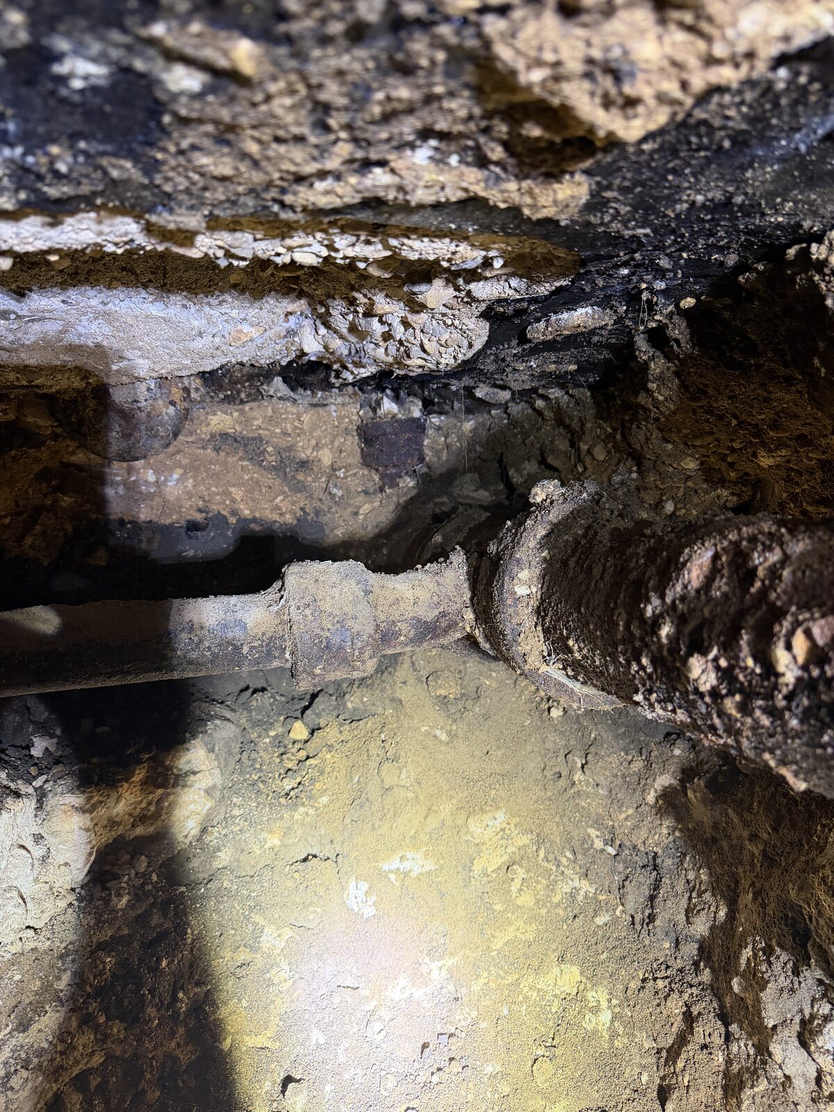 Cast-iron sewer line exposed in a tunnel dug beneath a slab foundation during under-slab plumbing repair
