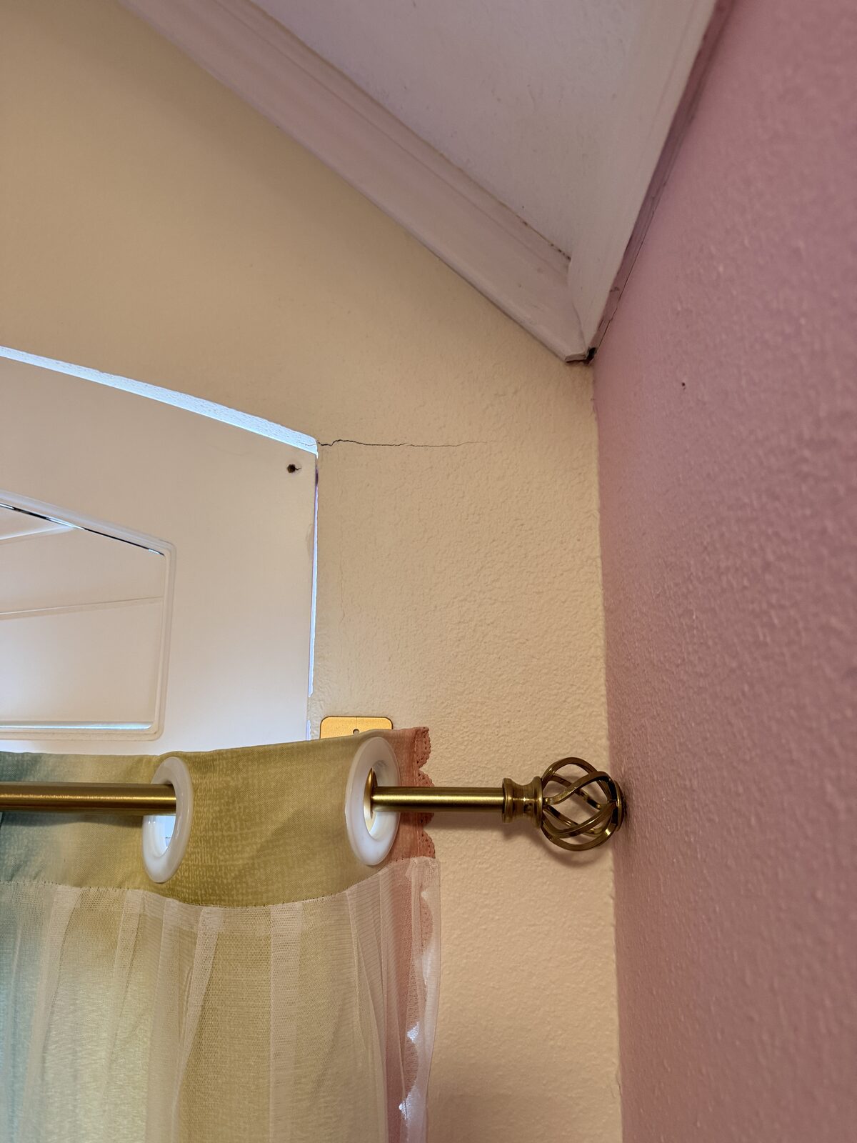 Crack along the ceiling line of a bedroom wall above the window, linked to foundation settlement
