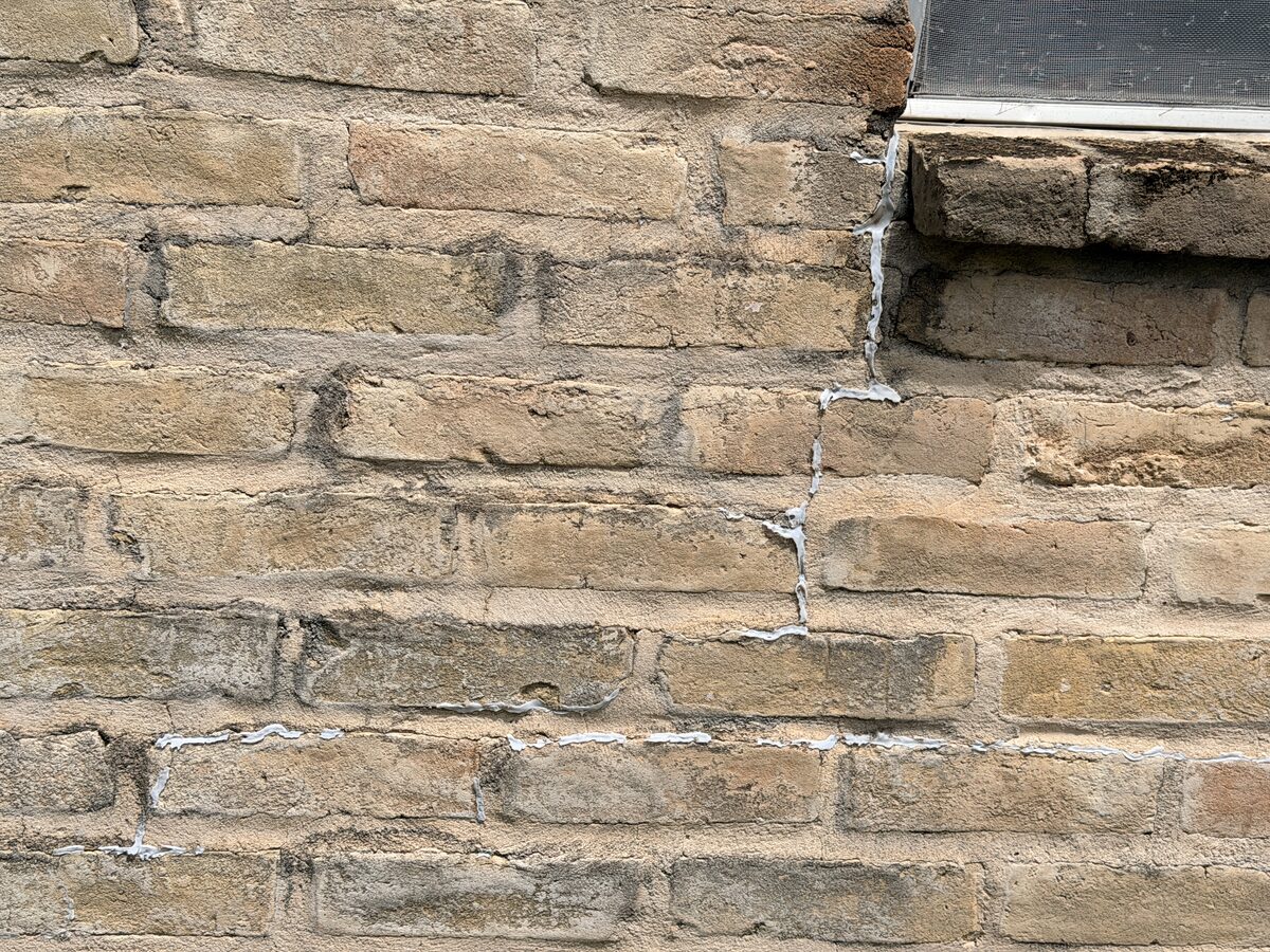 Close-up of cracked brick at a wall corner near a window sill, marked during a foundation inspection