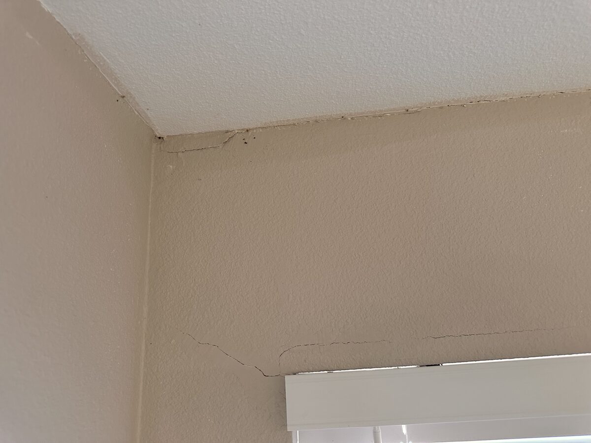 Crack climbing from window trim into the ceiling corner, an interior symptom of foundation movement