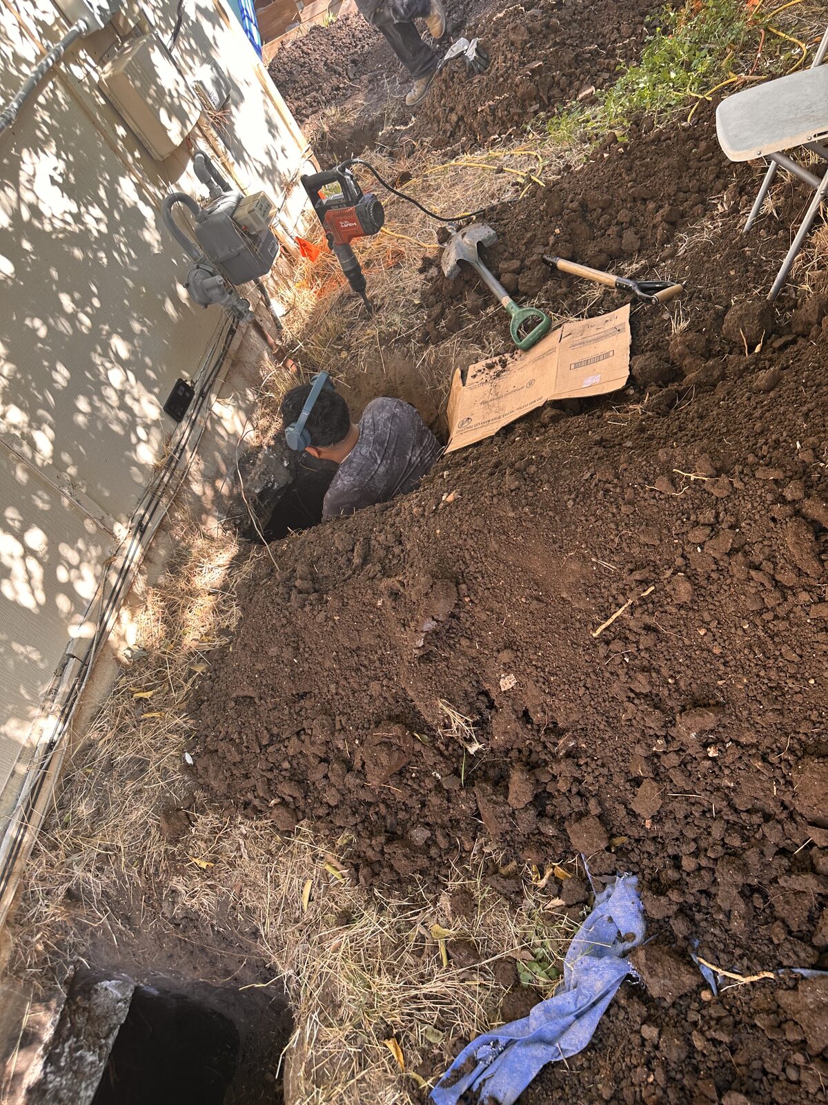Crew member working in a foundation access pit with tools and lumber staged at the surface