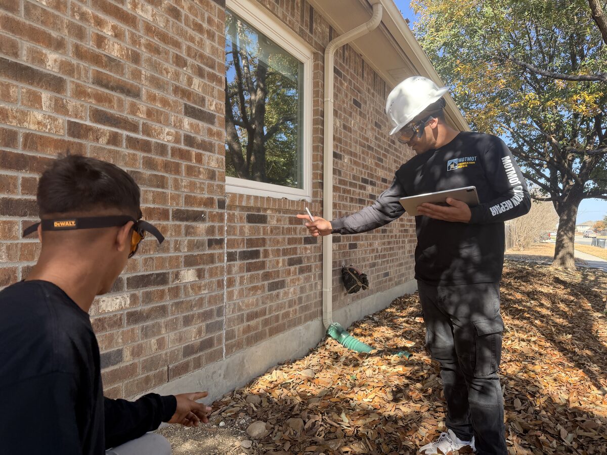 Two crew members inspecting brick veneer mortar joints for foundation settlement cracks