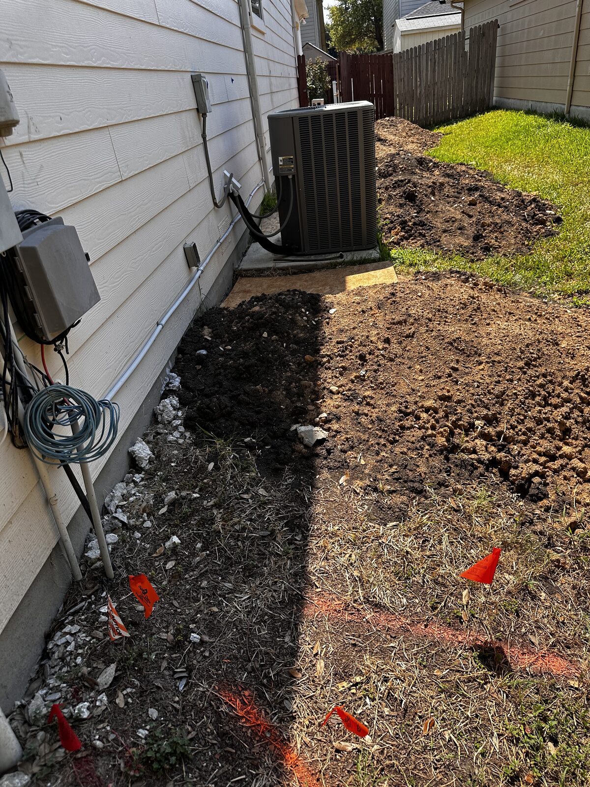 Excavated soil along a home's foundation with hydraulic hoses staged for pier installation