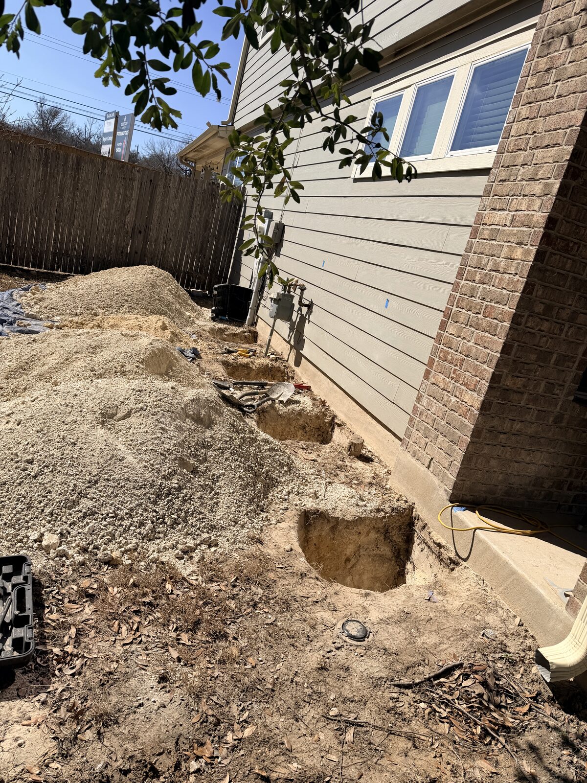 Soil piled along a home's exterior wall while the crew excavates footing access for foundation repair