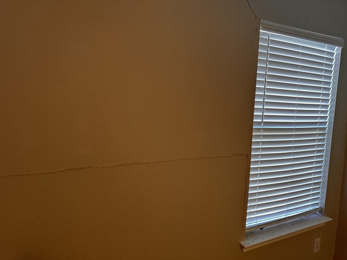 Faint diagonal crack in drywall next to a bedroom window flagged during a foundation inspection