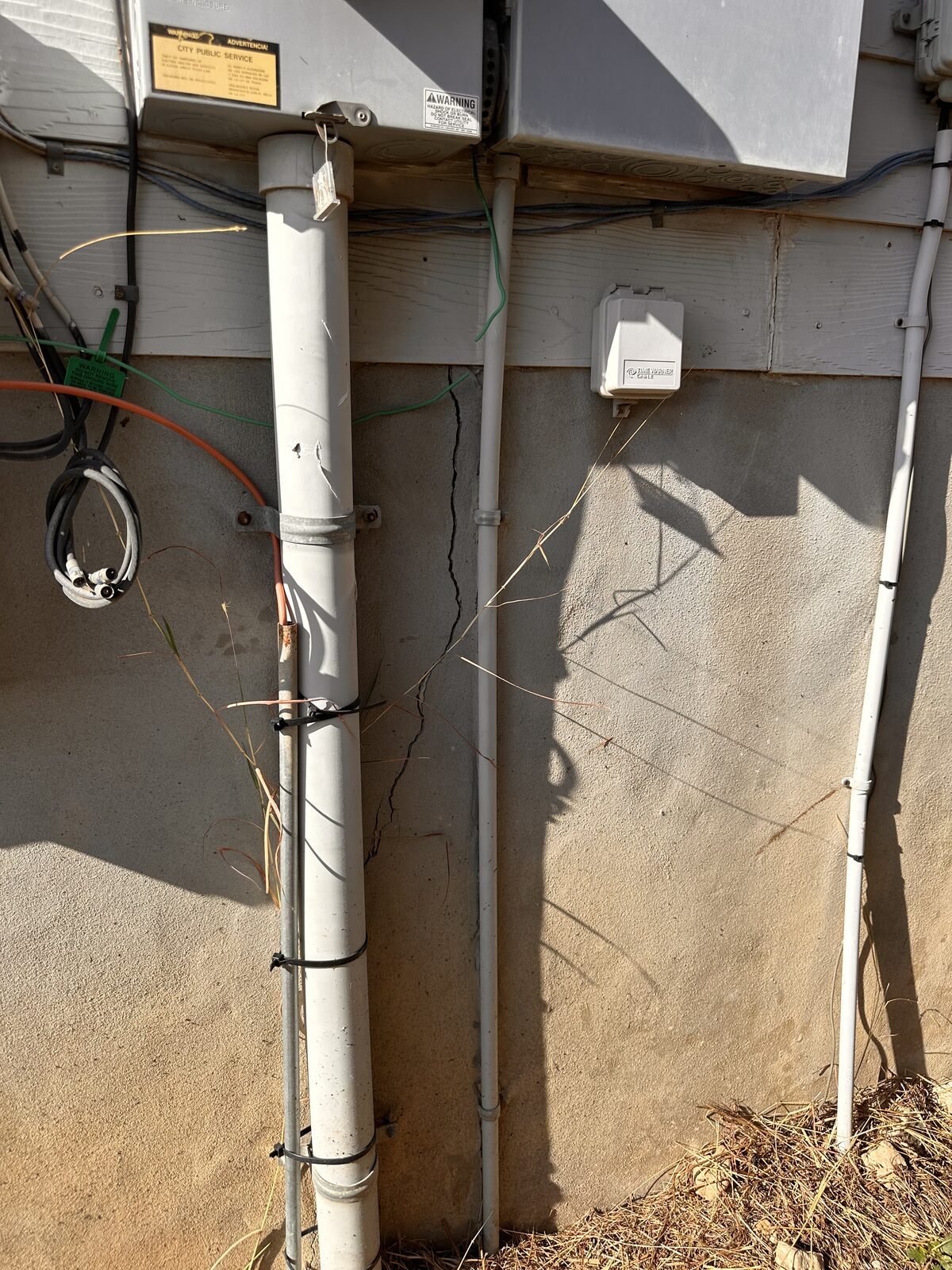 Hairline foundation crack behind utility pipes and conduit on a home's stem wall