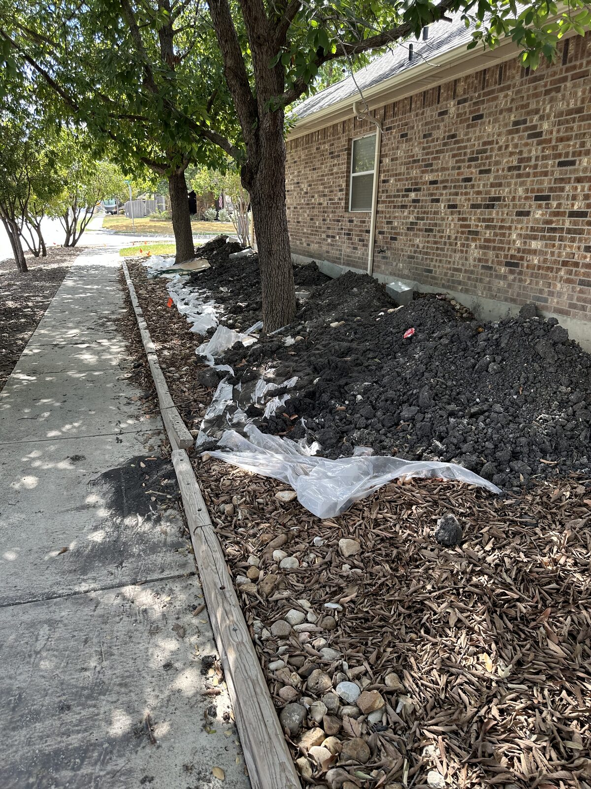 Foundation excavation spoil lining a brick home beside the sidewalk during pier installation
