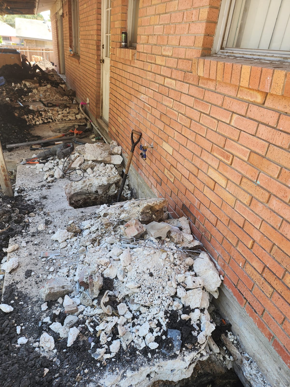 Excavation exposing the foundation of a brick home in Central Texas where steel piers are driven beneath the grade beam