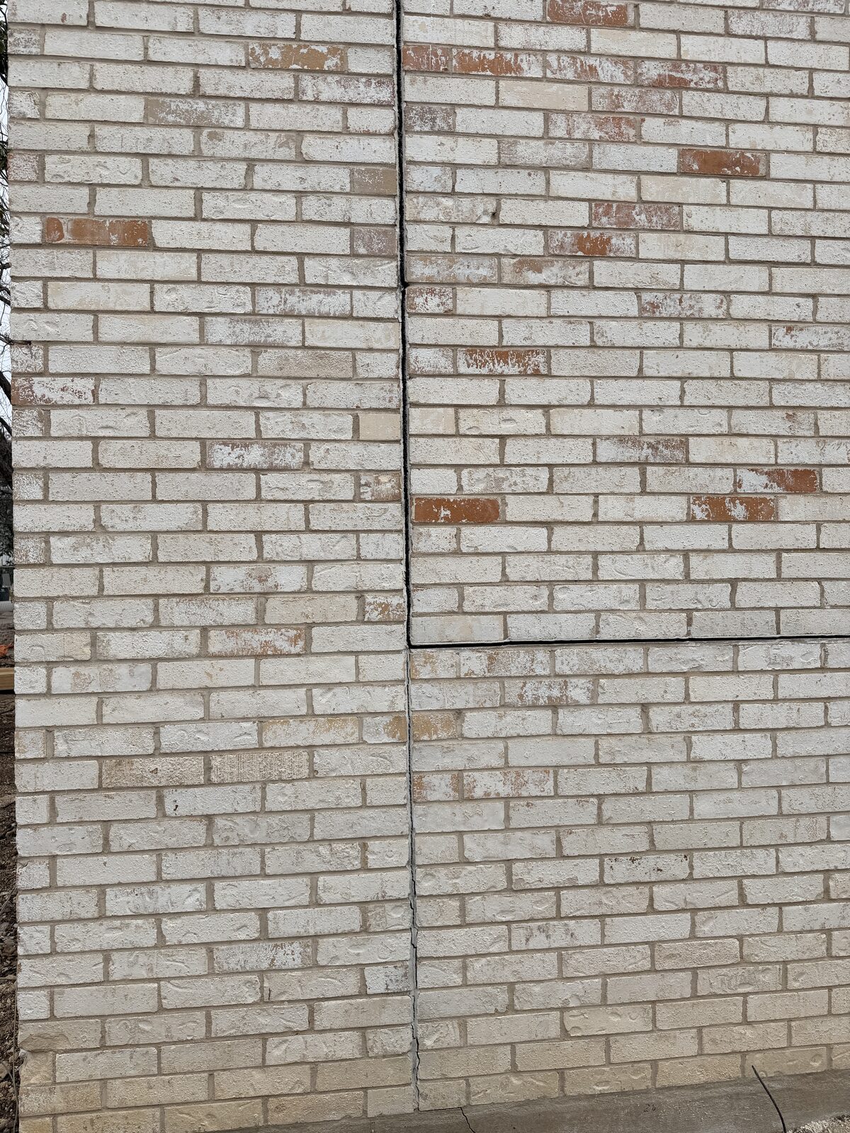 Full-height brick wall showing repointed vertical and horizontal crack lines after foundation repair