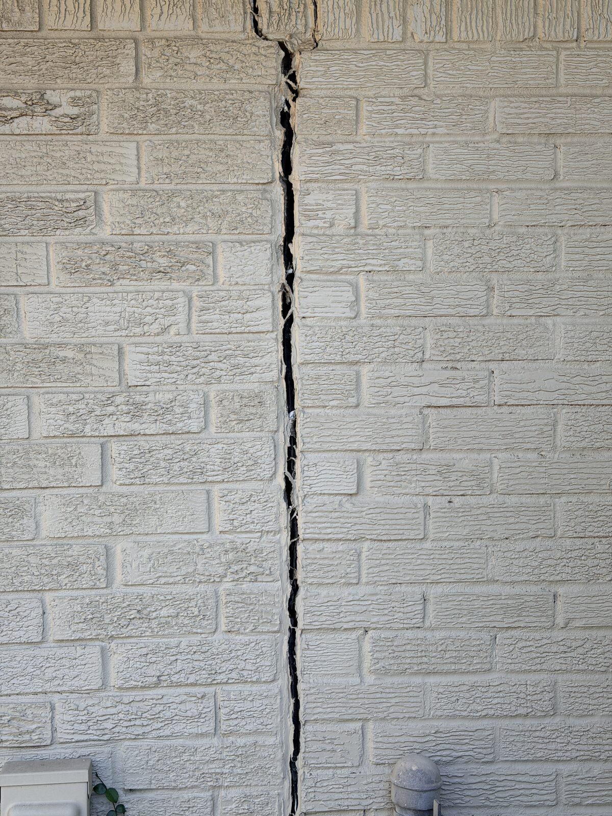 Full-height vertical crack through painted brick veneer caused by foundation settlement