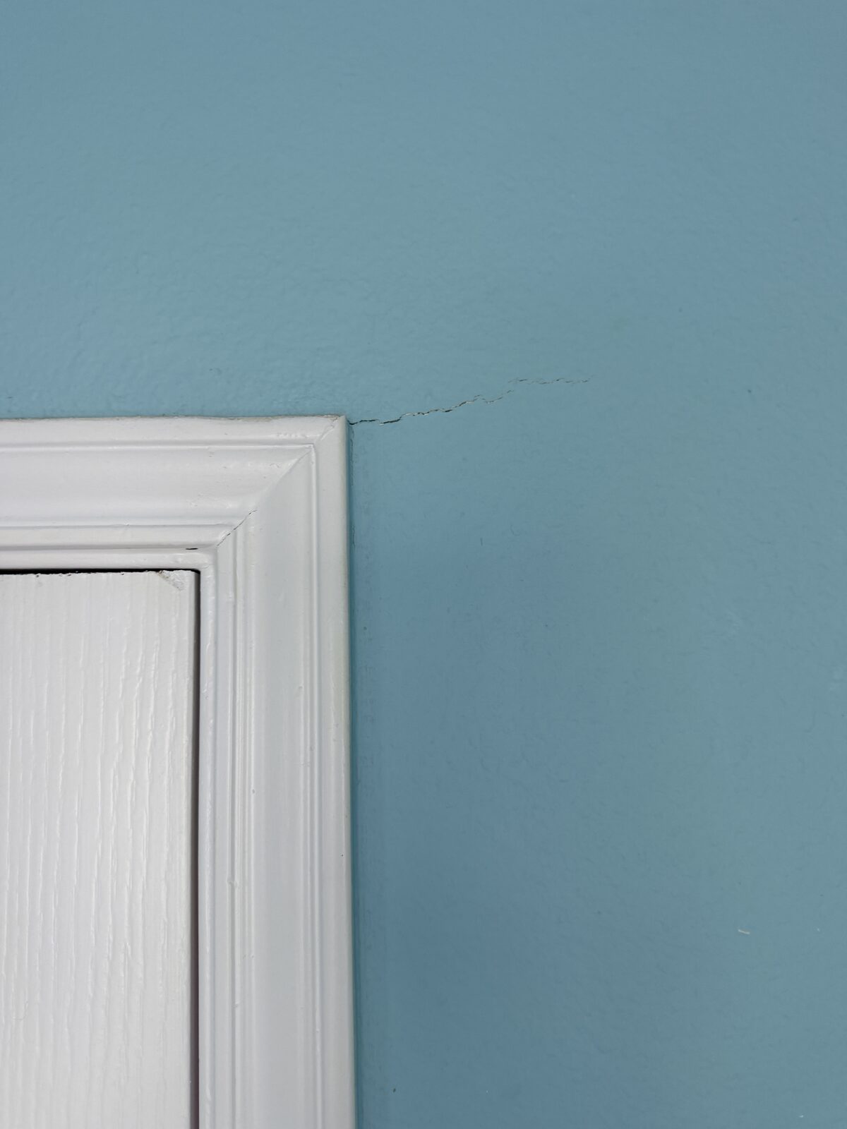 Hairline crack extending from a door trim corner on a blue wall during a foundation inspection