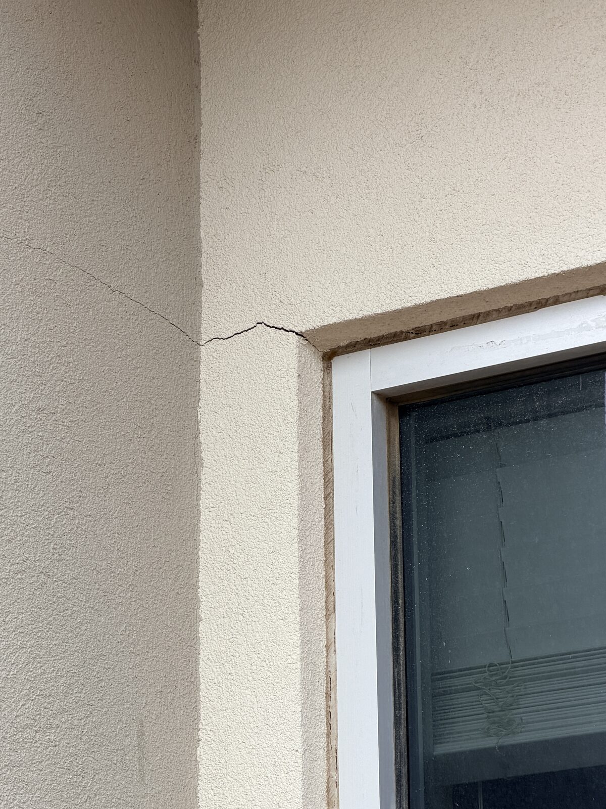 Hairline crack at the header corner of a window in a white stucco wall, documented during a foundation assessment