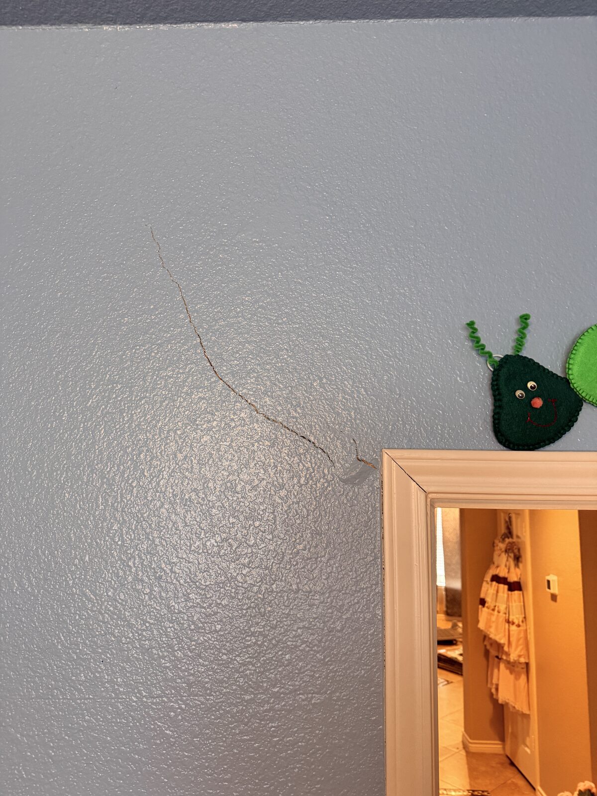 Hairline crack spreading across a bedroom wall corner above a closet door, checked during a foundation inspection