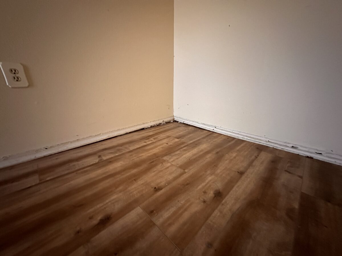 Interior corner showing baseboard separation above vinyl plank flooring in a settling home