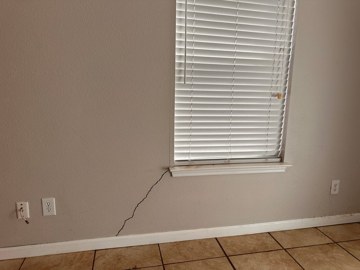 Diagonal drywall crack running from a window corner toward the baseboard, a common interior sign of foundation movement