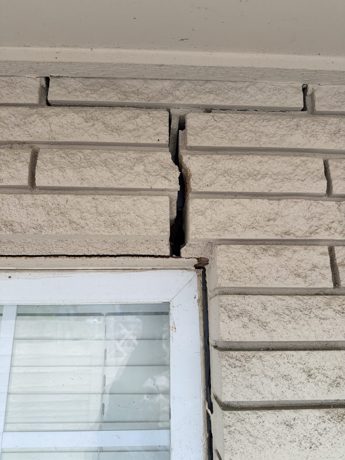 Stone veneer lifted and cracked above a window corner from differential foundation settlement