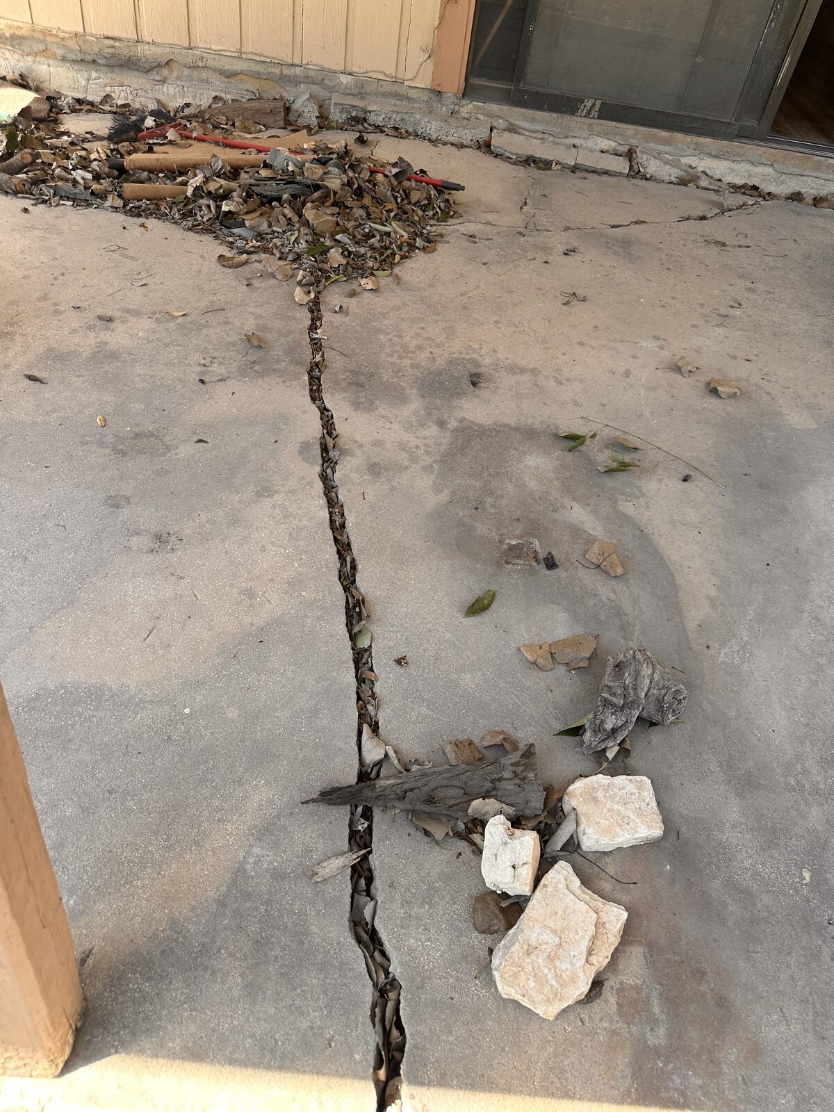 Long crack splitting a backyard concrete patio slab, with loose rubble along the break