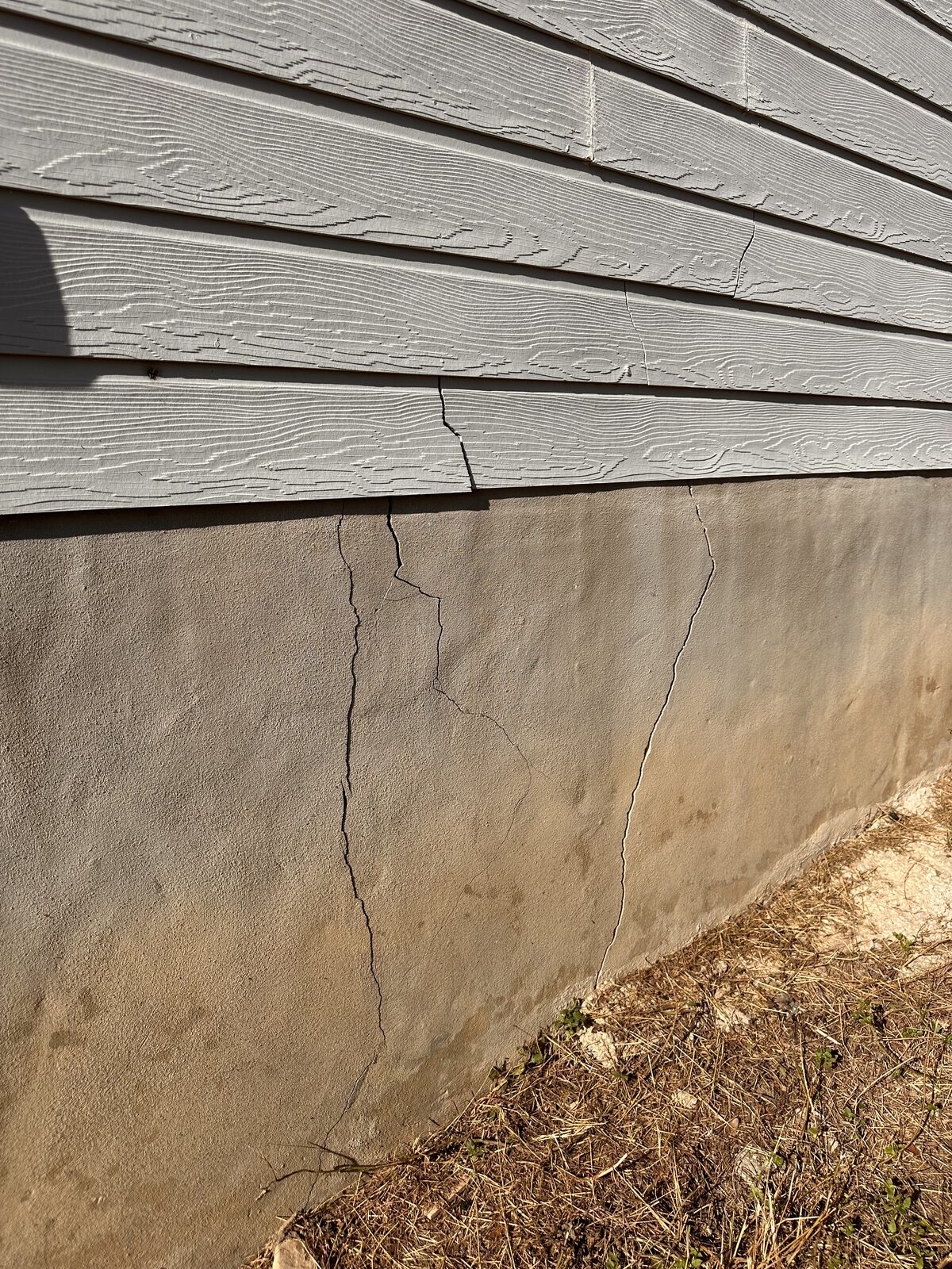 Long vertical crack descending a concrete stem wall beneath gray lap siding