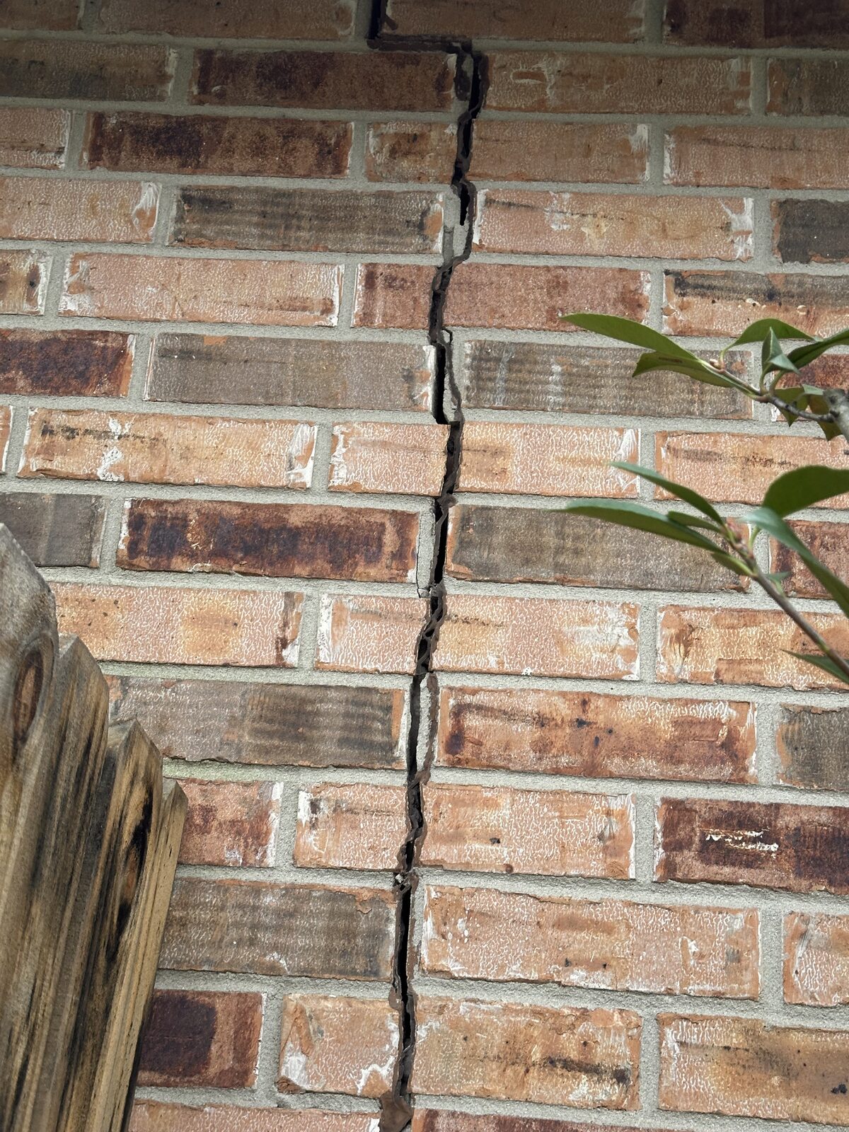 Long vertical crack splitting brick veneer at a home's corner, indicating differential foundation settlement