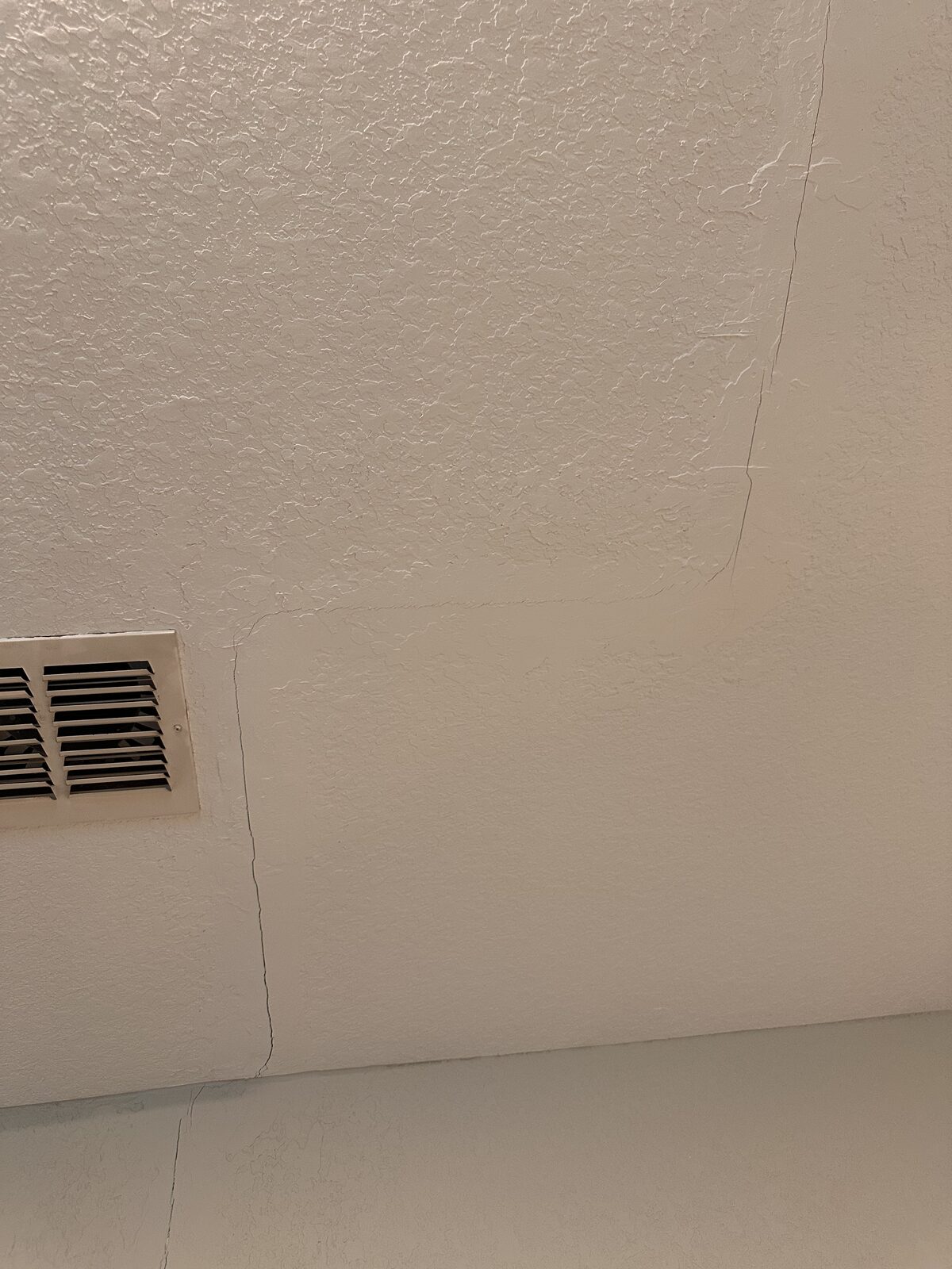 Previously patched drywall crack near a ceiling air vent, evidence of past foundation movement