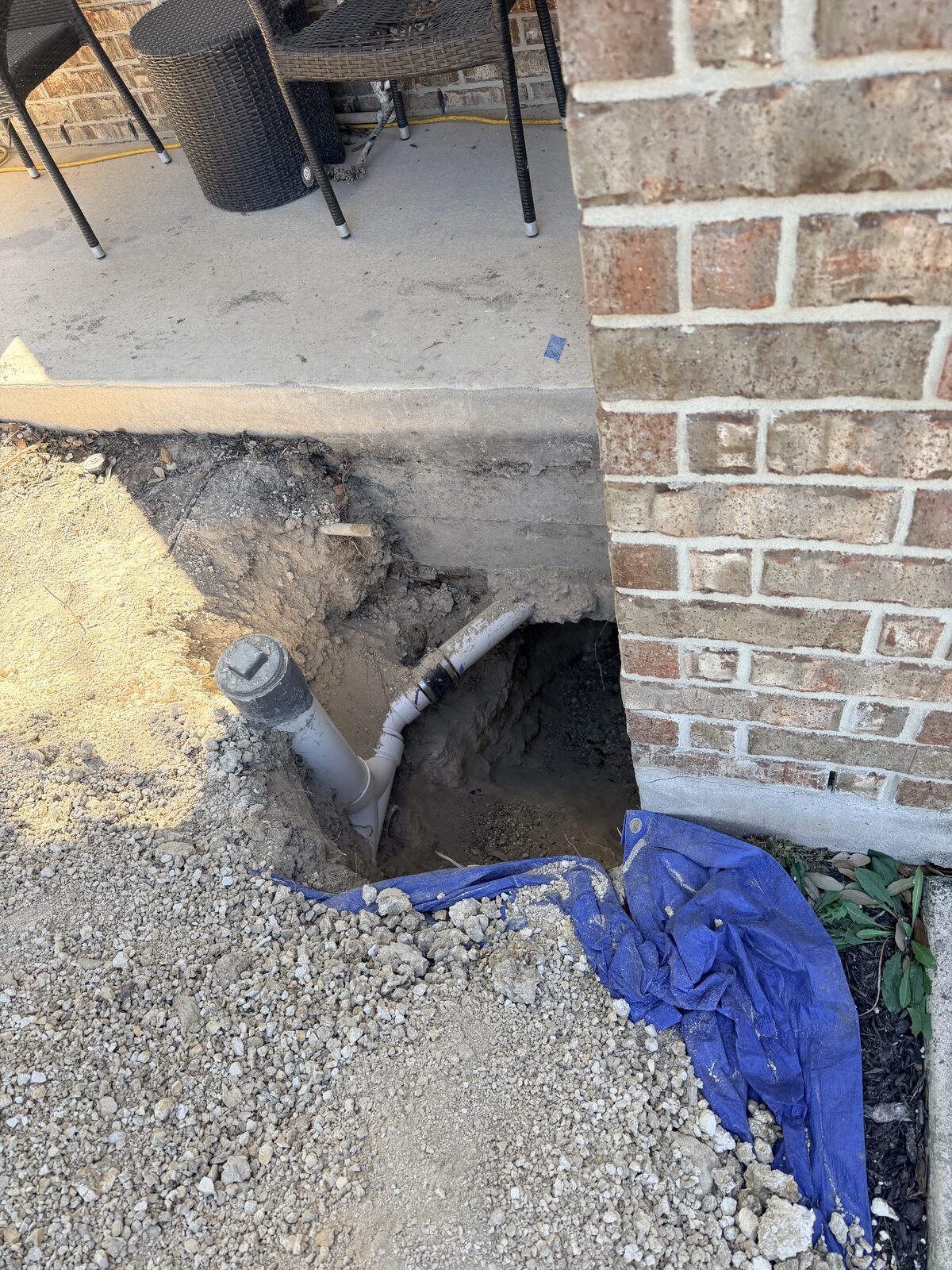 Hand-dug pier hole exposing the slab edge at a brick home's porch corner during foundation repair