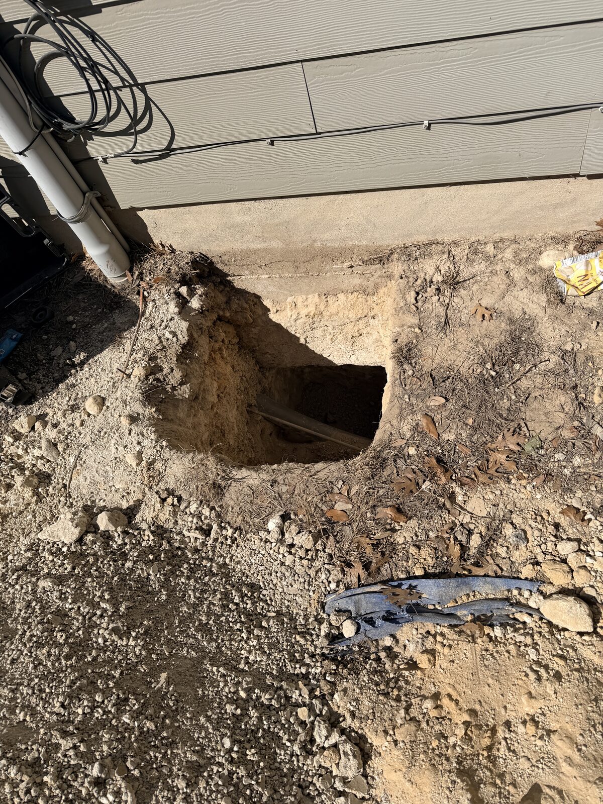 Excavated foundation pier pit beneath an exterior wall with utility conduits routed safely overhead