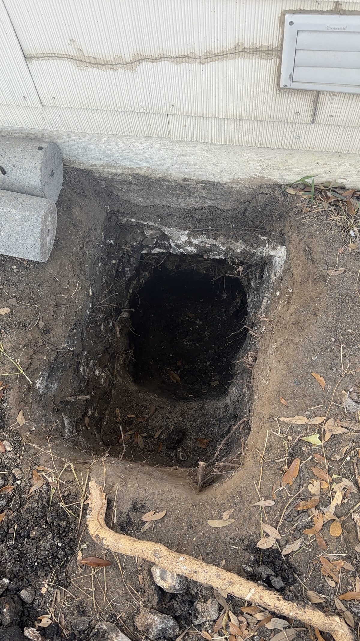 Square pier pit dug beneath a slab edge with the plumbing line carefully exposed during repair