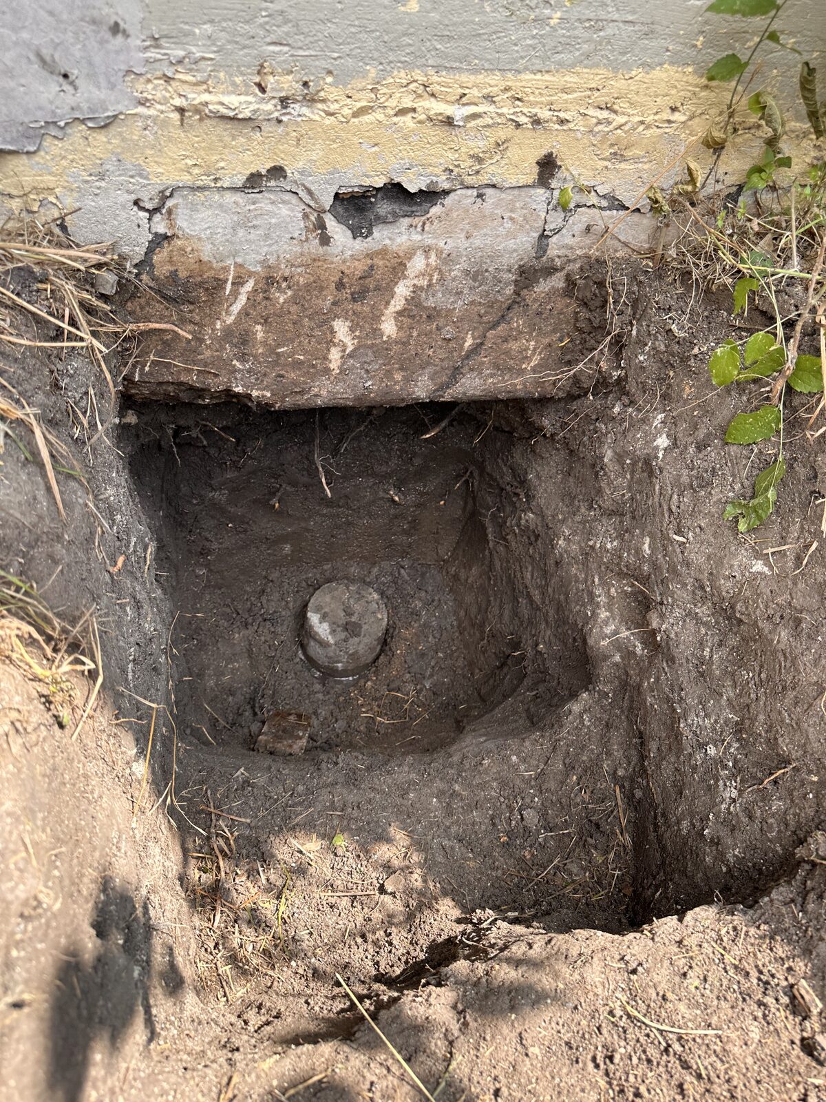 Pressed pile head visible in an open pier pit at the edge of a home's foundation during underpinning