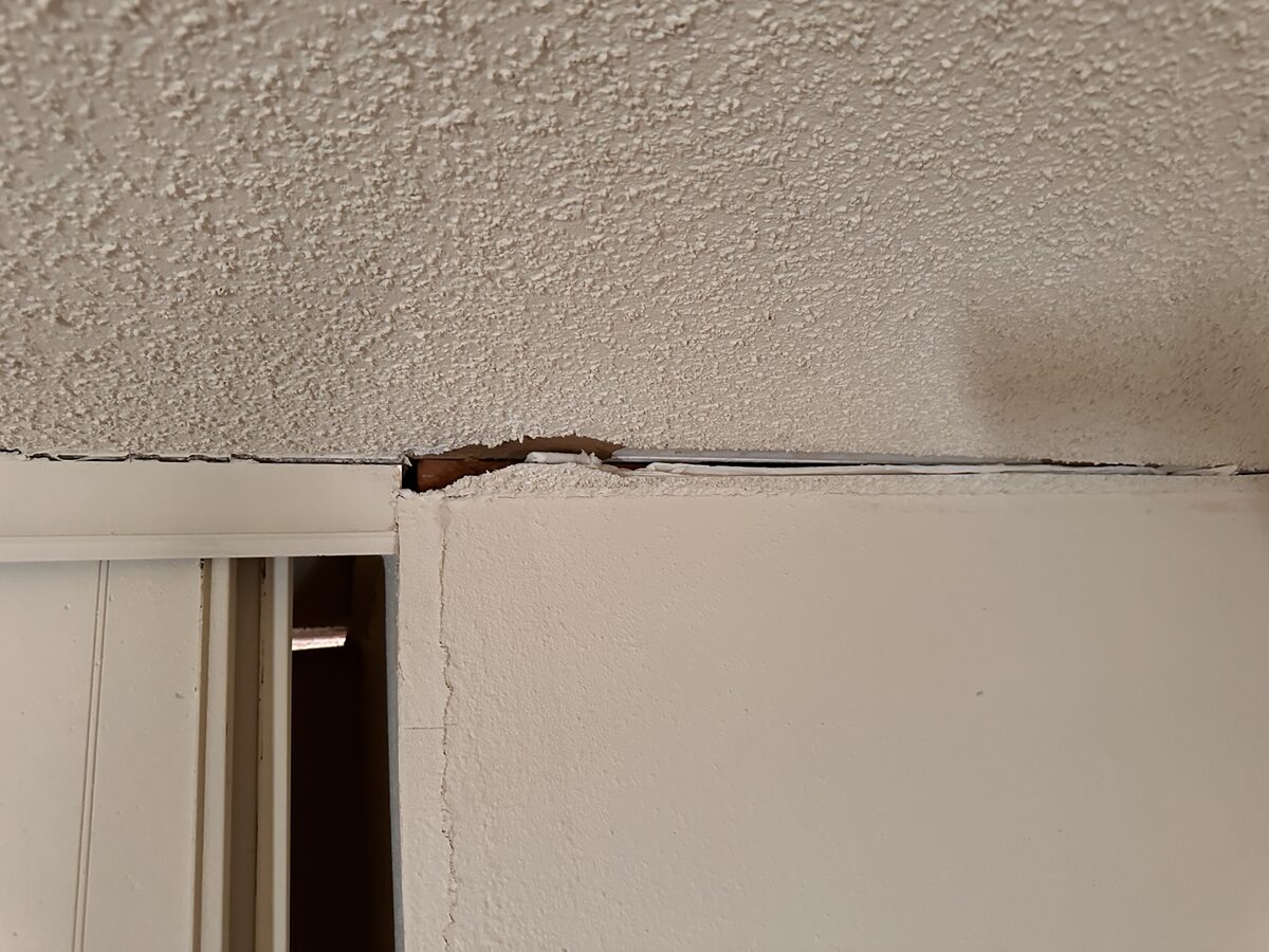 Dark separation gap at the ceiling trim above a door frame from ongoing foundation settlement