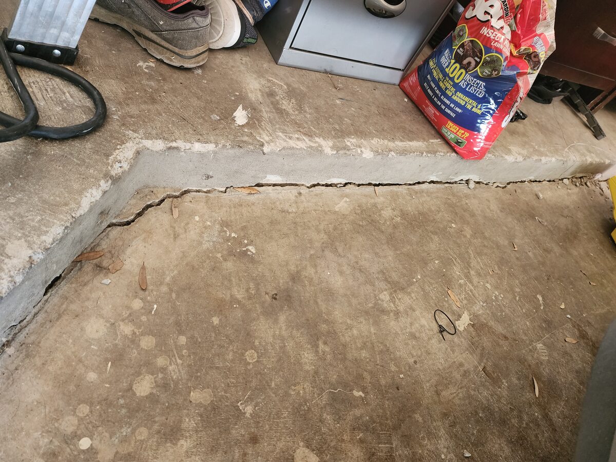 Wide separation gap along a settled garage slab joint, showing foundation settlement before repair