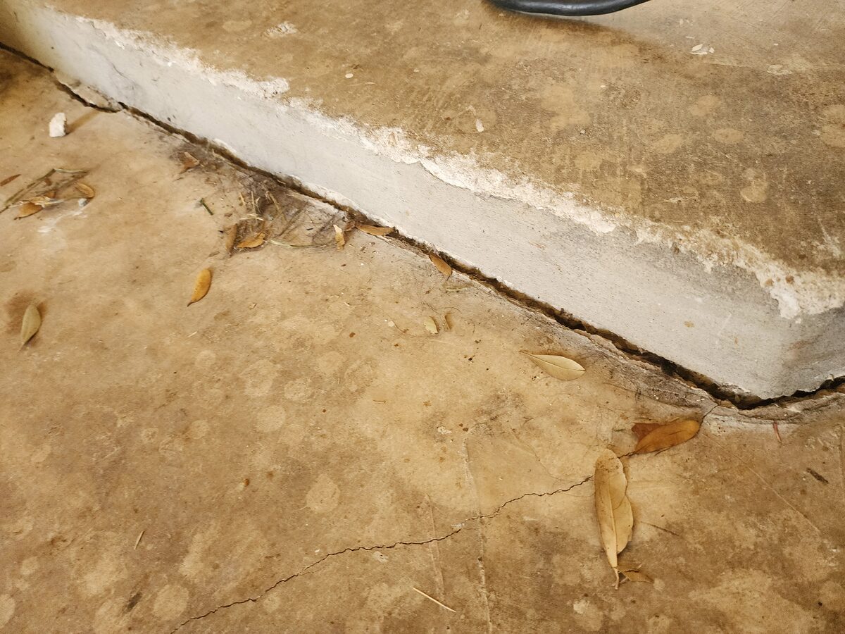 Close-up of a settled concrete slab step with a visible gap, photographed during a foundation repair assessment