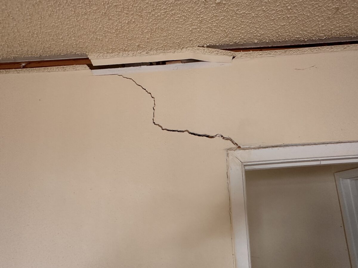 Stair-step crack tracking along the ceiling line near a doorway in a settling house