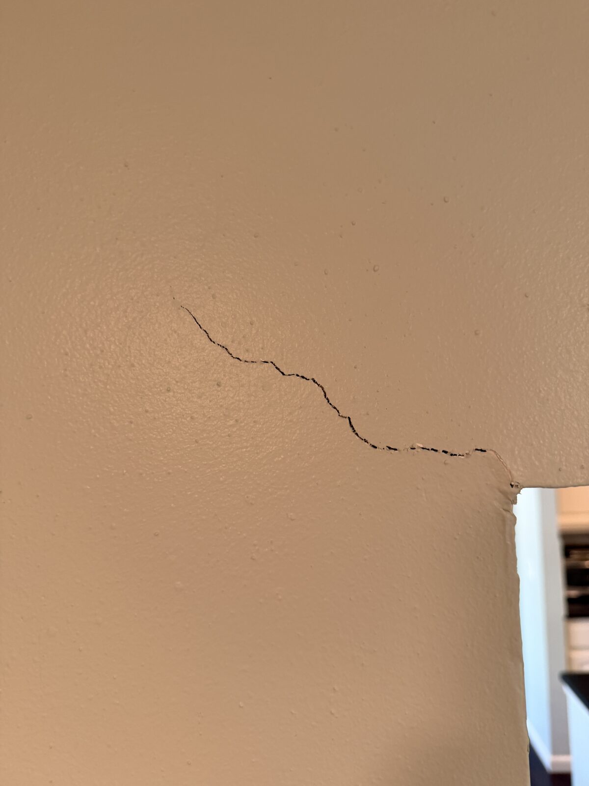 Closeup of a stair-stepping drywall crack meeting a door frame corner before foundation repair