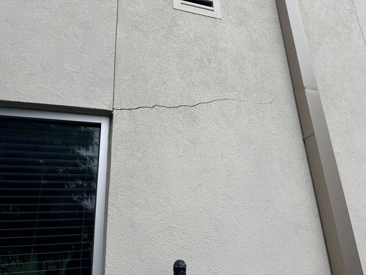Settlement crack extending from a window corner across a stucco wall near a downspout
