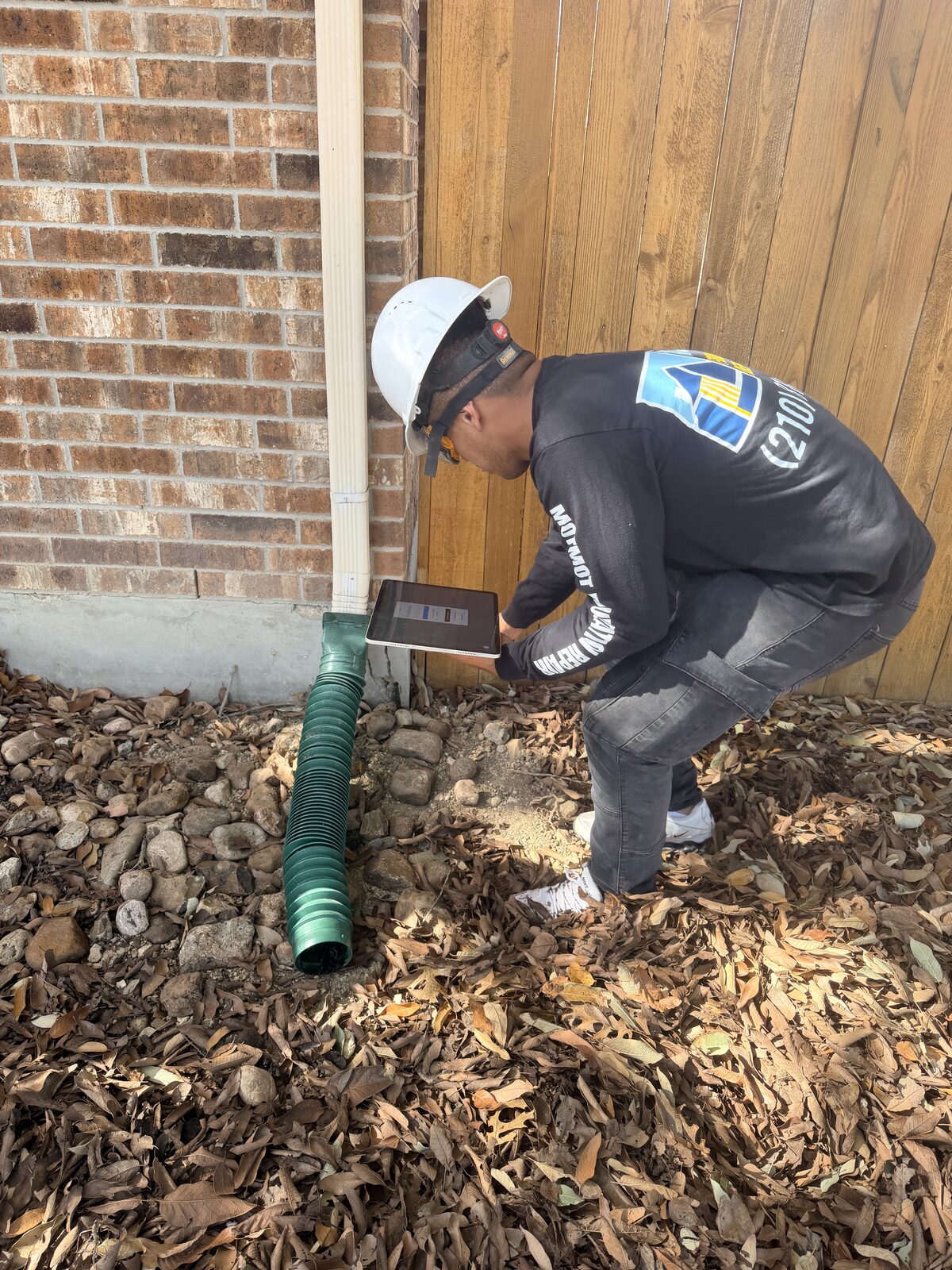 Technician photographing a flexible downspout extension at the slab edge during a drainage evaluation