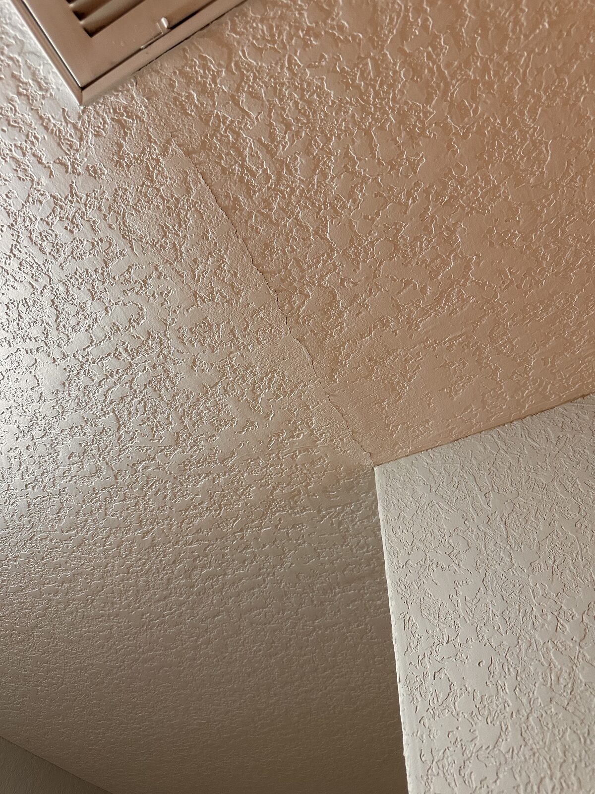 Crack along a textured ceiling seam at an interior corner caused by foundation settlement