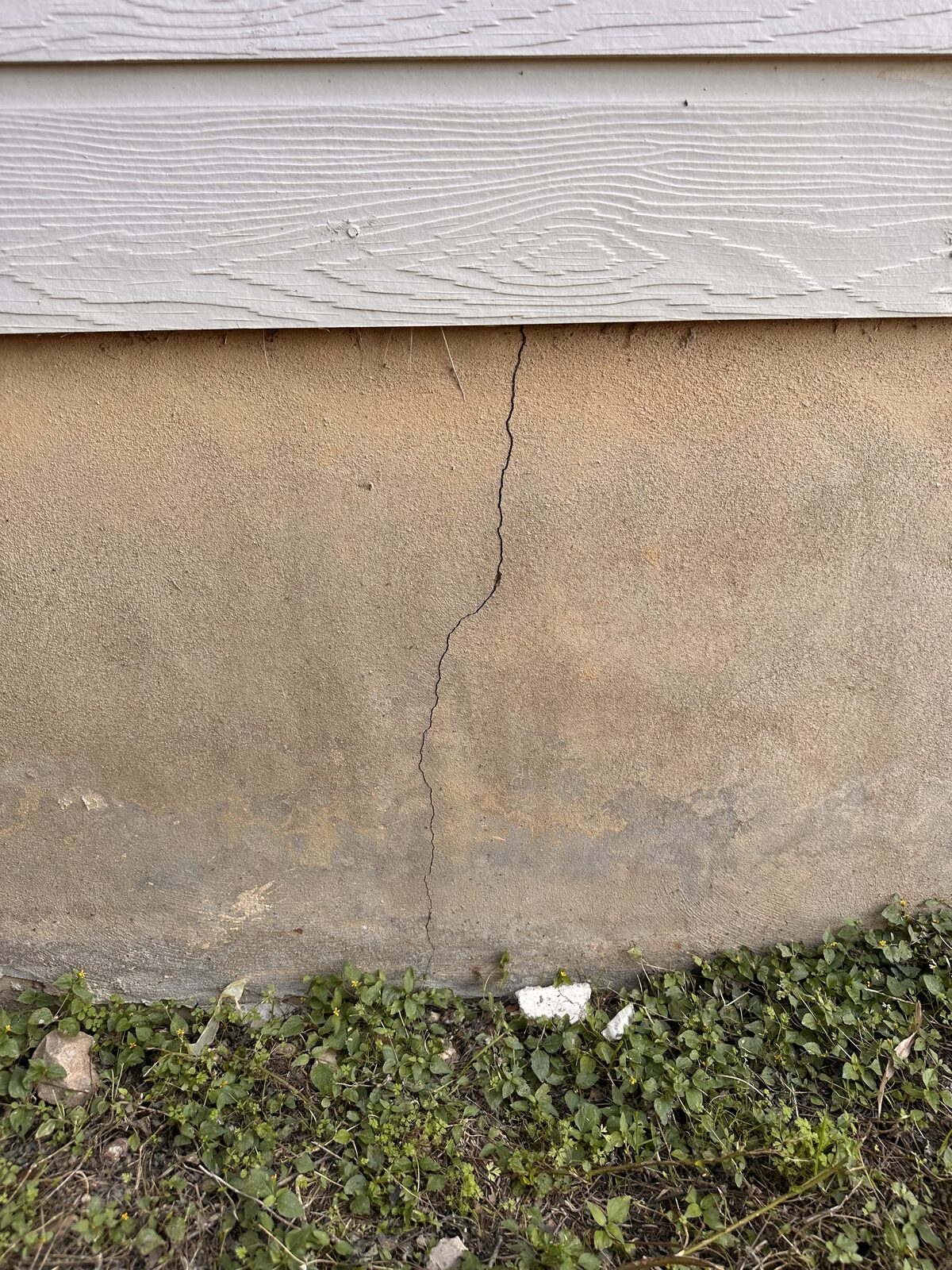Thin vertical crack in a home's parged stem wall just below the siding line