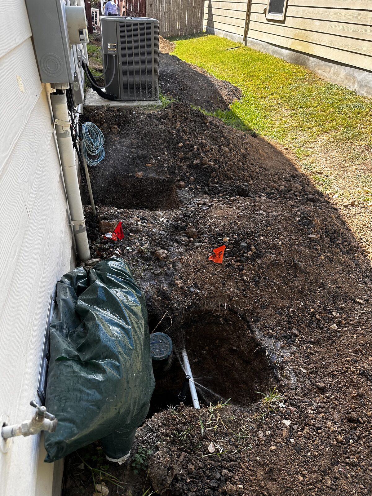 Trench excavated along a home's foundation with bagged soil staged for backfill during pier work