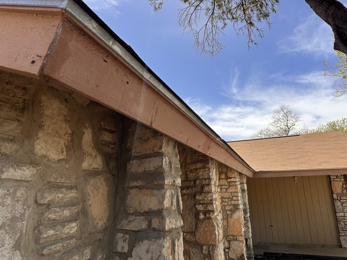 Sagging roofline and fascia above a stone-veneer wall, an exterior sign evaluated during foundation inspections