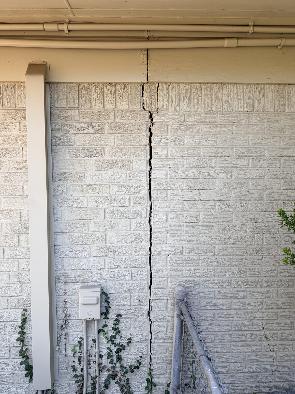 Vertical settlement crack splitting a painted brick wall beside a downspout before foundation repair