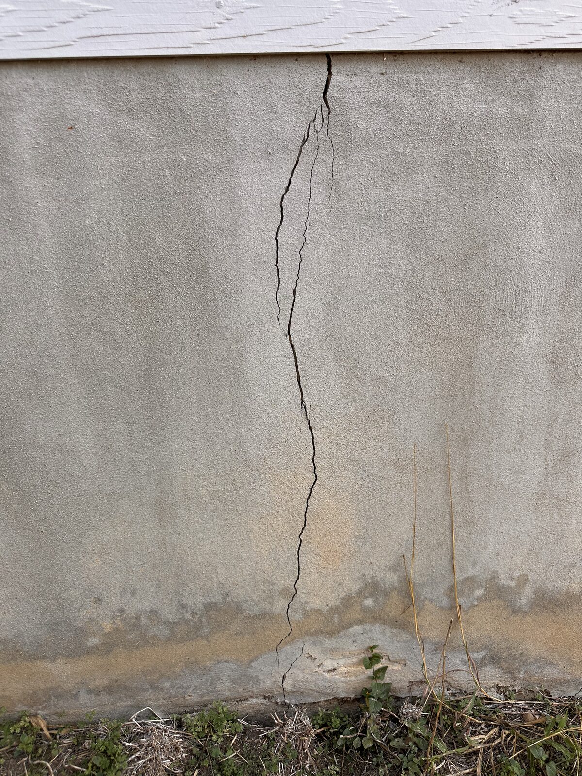 Long vertical foundation crack with staining at the base of a parged stem wall