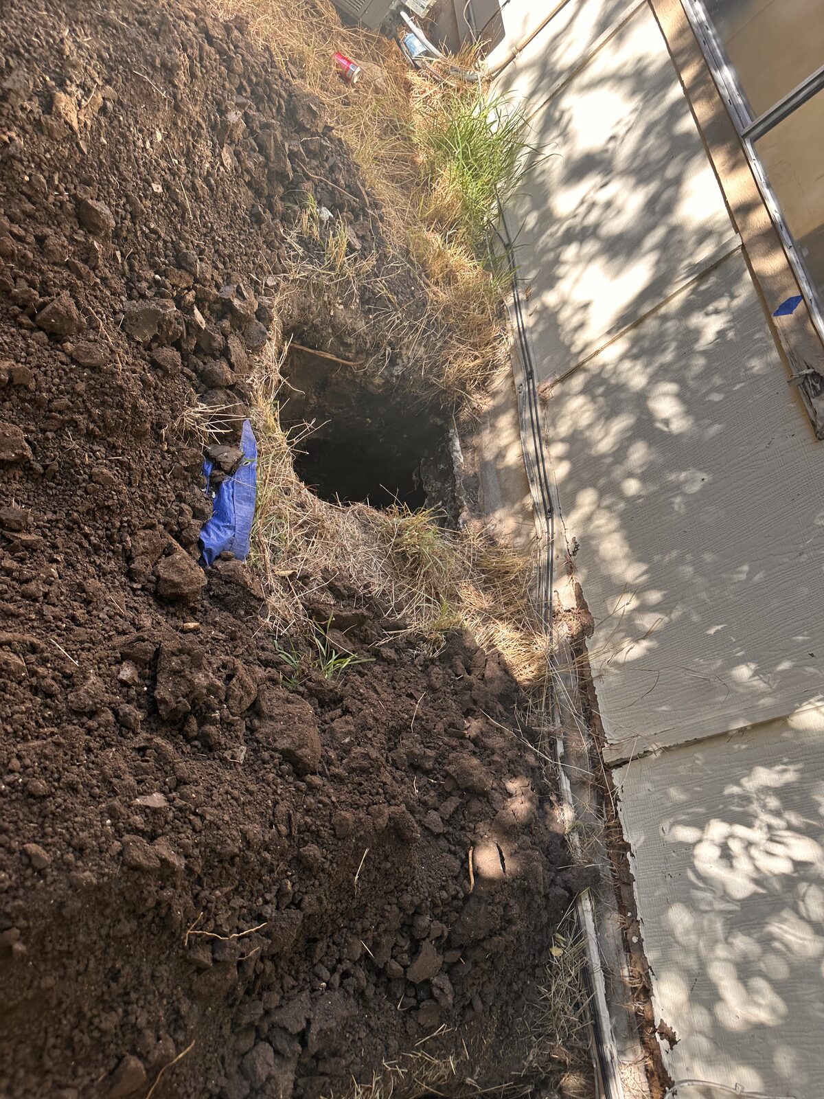 Excavation along a concrete walkway opening into a tunnel under the home's foundation
