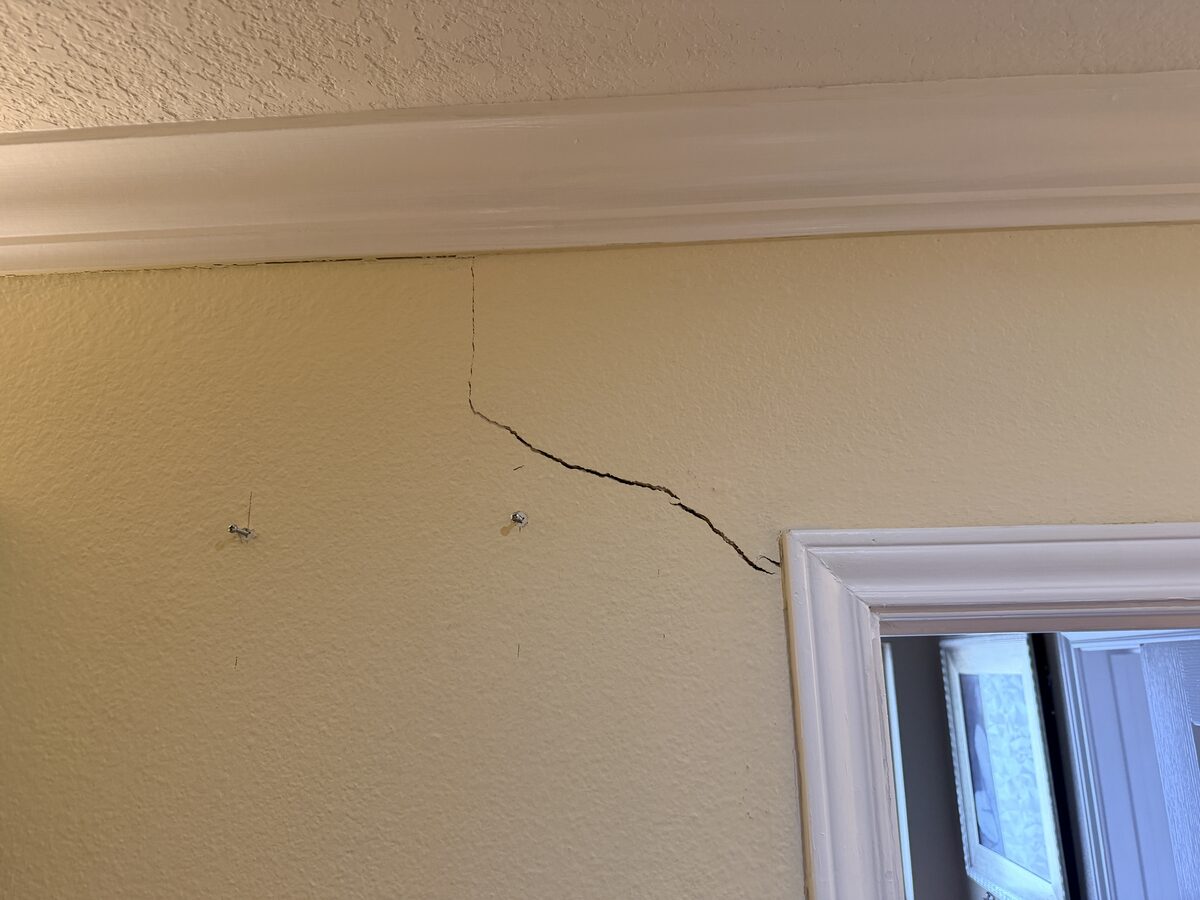Drywall crack spreading from a frame corner toward the crown molding, a sign of foundation settling